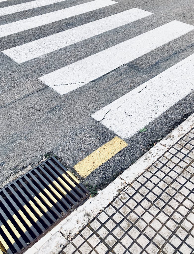 Crosswalk marked on asphalt road near sewer grid in city